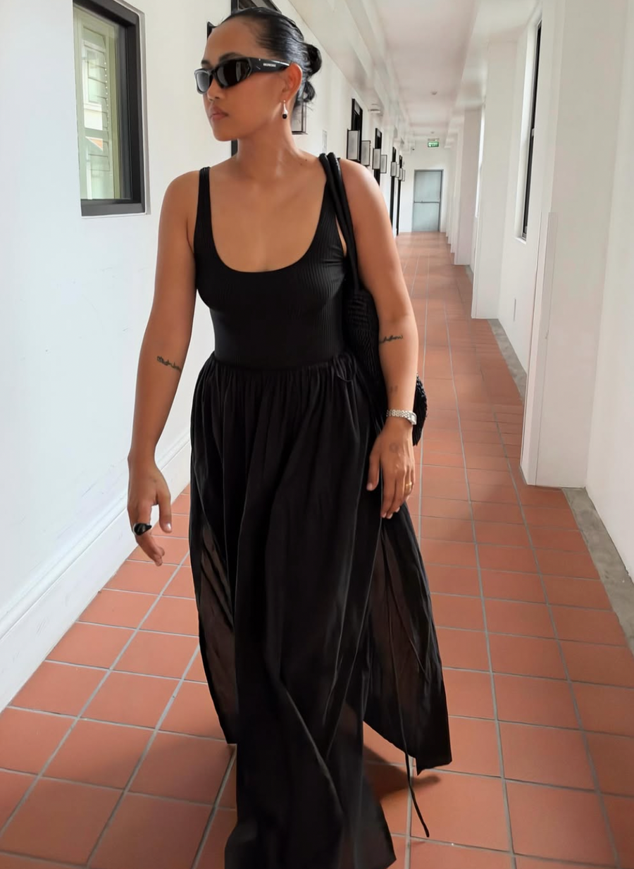 Ri walking down a tiled corridor in the Maya skirt in Black with a black scoop-neck tank