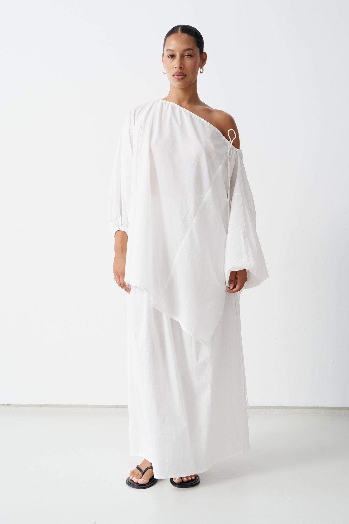 Model wearing the Joss blouse off one shoulder over the Maya maxi skirt, both in White