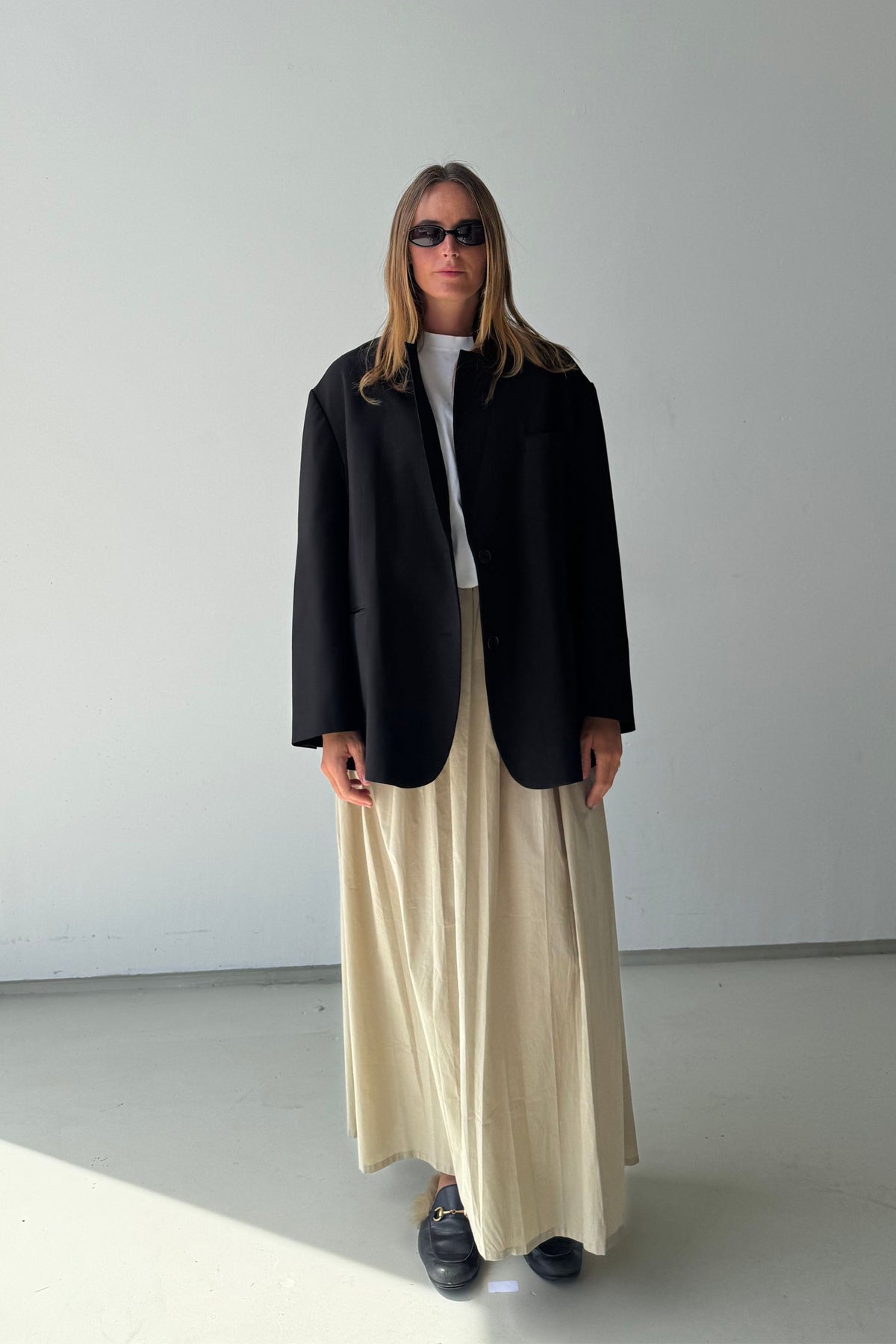 Woman wearing the Maya maxi skirt with an oversized black blazer, white tee and loafers in a studio